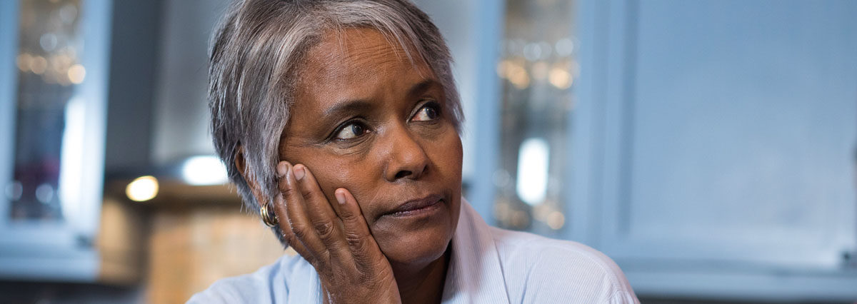 Older woman of color looking pensively off into the distance with her head propped up by her hand