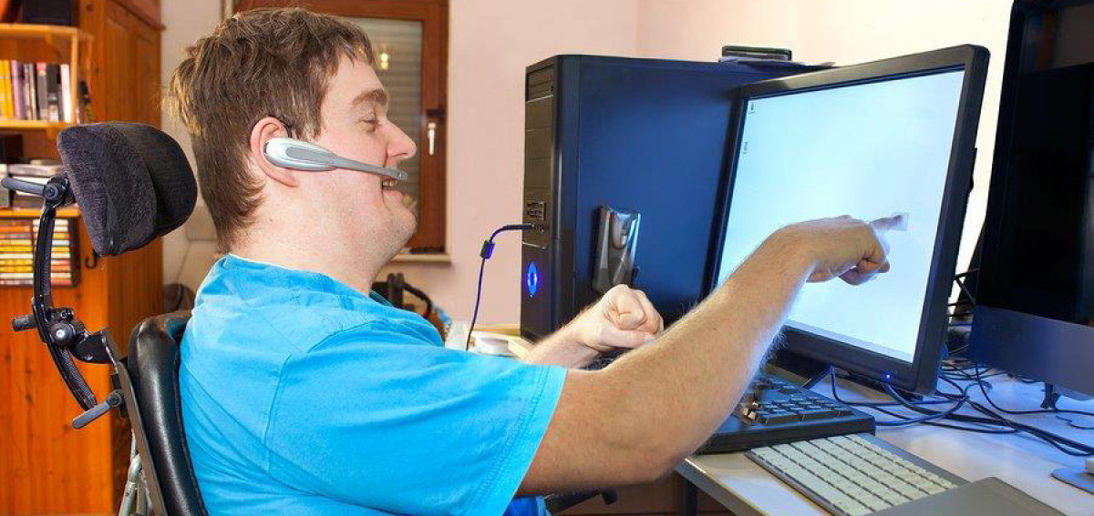 Middle-aged white male living with a disability is happily working at his computer and pointing at the monitor