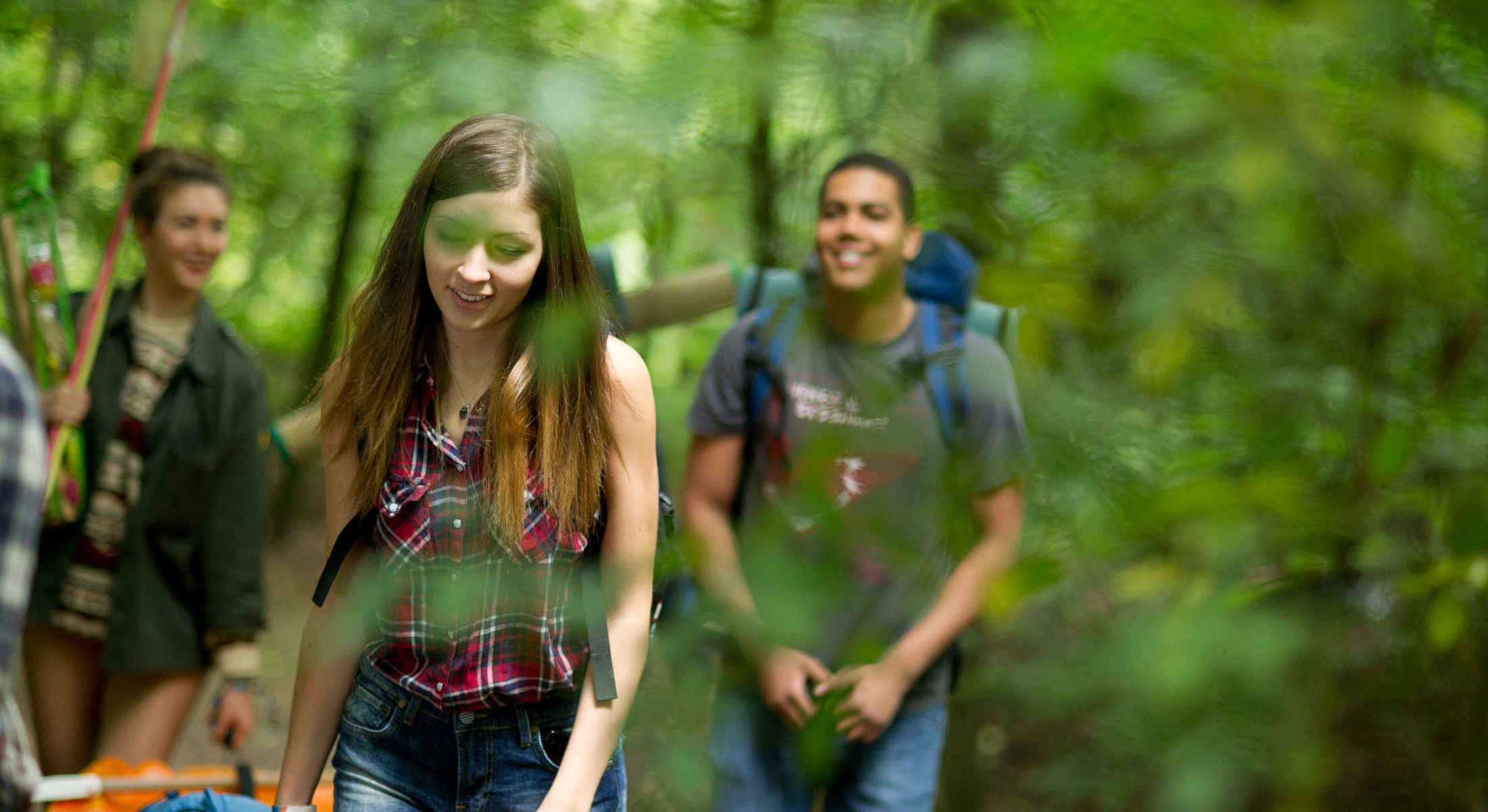 Group of teens smiling, exploring outdoors with backpacks and camping items