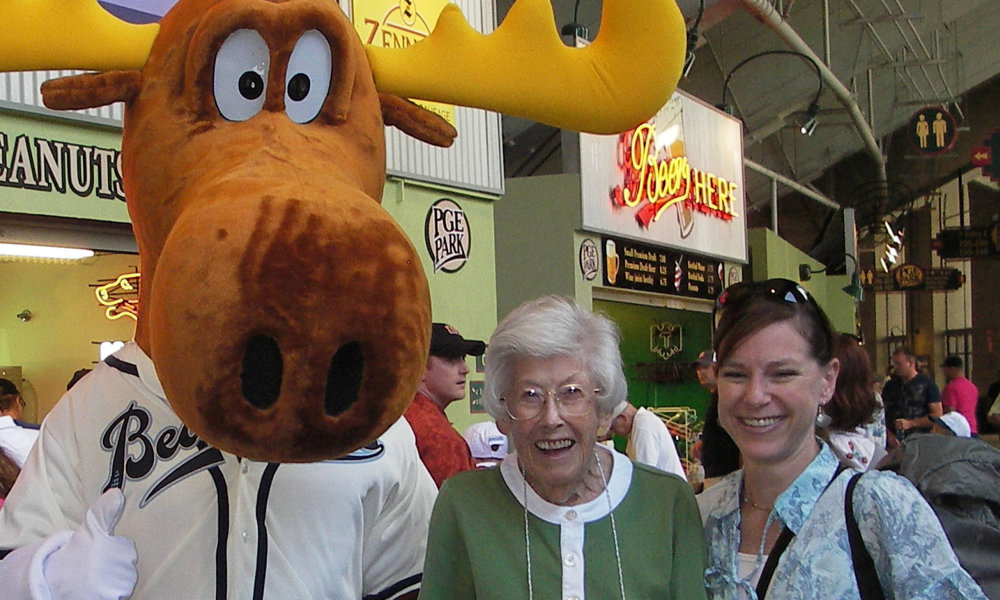 Middle-aged female adult in sports stadium with senior mother and moose mascot, smiling at camera