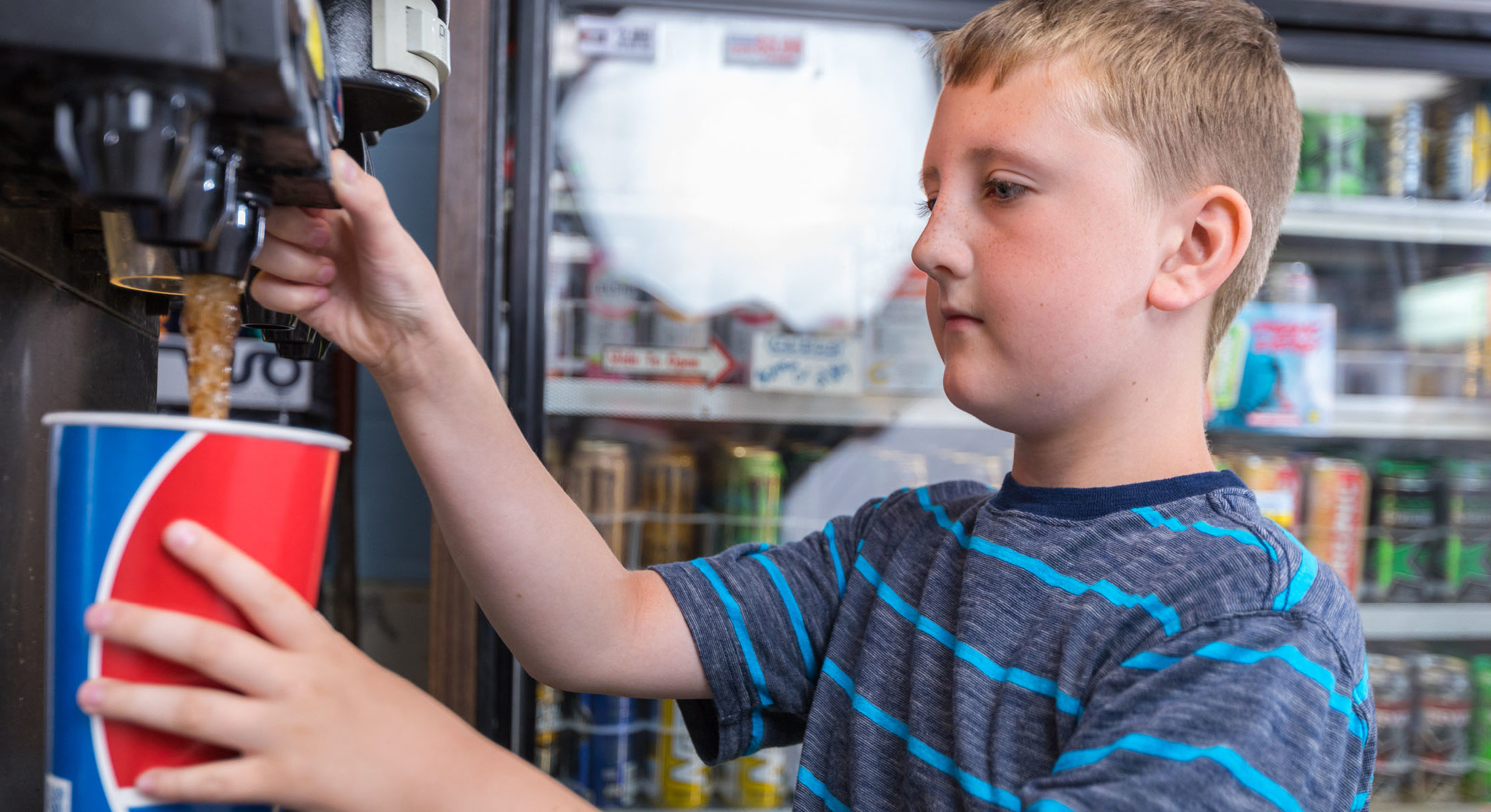 white male kid filling very large soda inside conveinece store