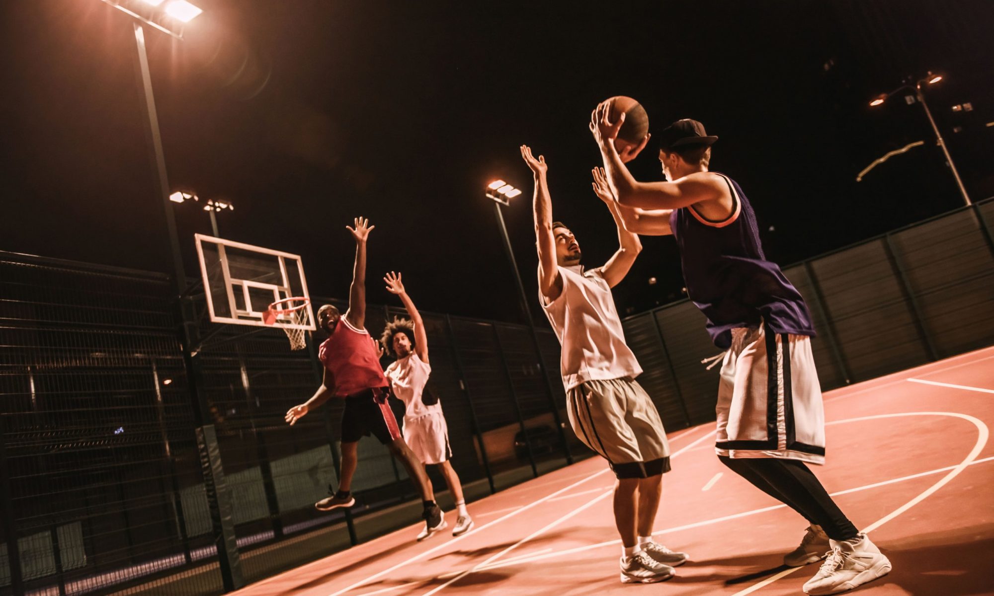 Young male adults playing basketball outside at night