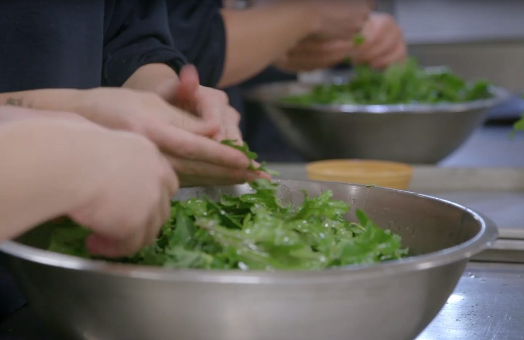 Hands making salads inside at an organization
