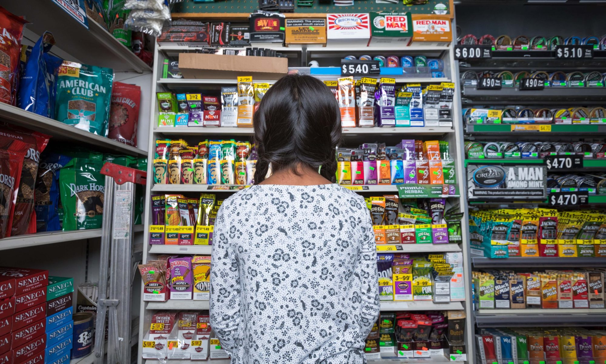 Looking at power wall full of colorful tobacco products in a convenience store from behind a young female child with pigtails